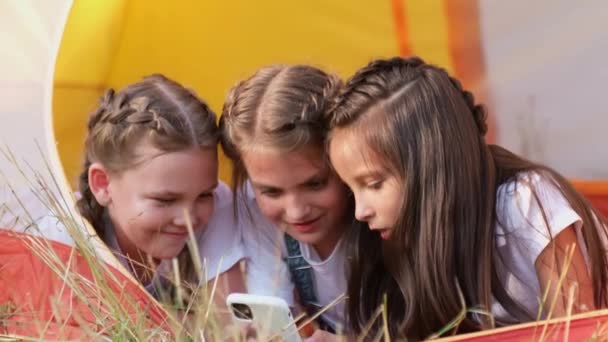 Glada flickor som använder smartphone liggande i ett tält. — Stockvideo