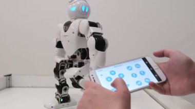 Beyaz robot bir dizi hareketini gösteriyor. Bir kız sergide bir insansı robotu kontrol ediyor..