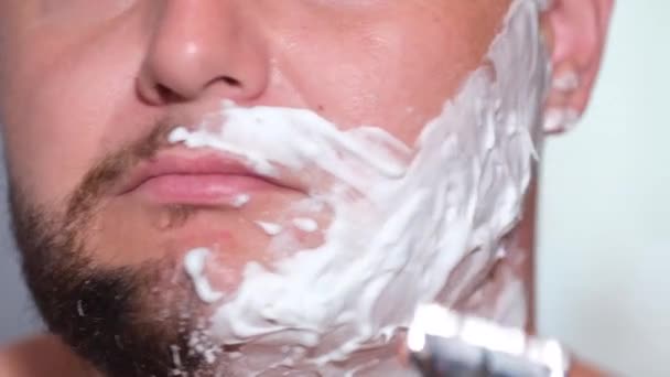 Молодой человек сбривает бороду острым лезвием. — стоковое видео