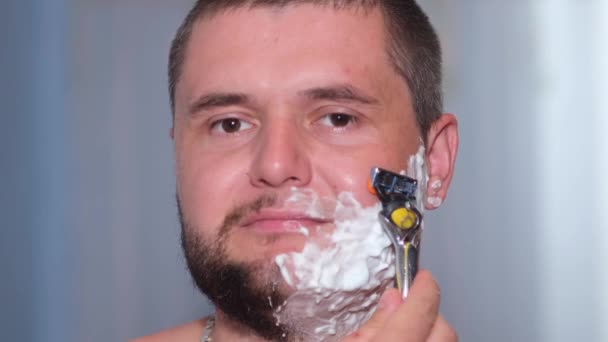 Un homme avec de la mousse sur le visage se rase la barbe. — Video