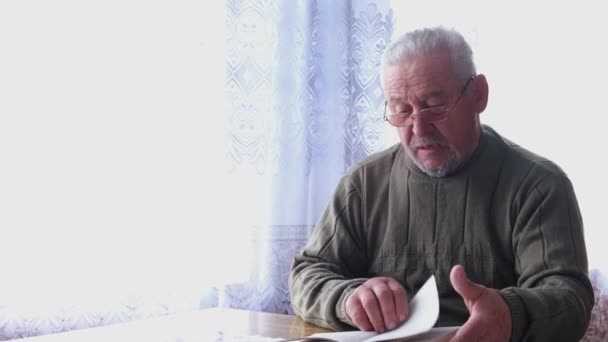 Un nonno dai capelli grigi legge un libro con una lente d'ingrandimento — Video Stock