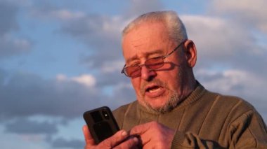Gülümseyen yaşlı adam akıllı telefonla konuşuyor..