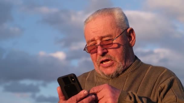 Souriant vieil homme bavarder avec smartphone. — Video