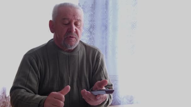 Un grand-père âgé commute les chaînes de télévision avec une télécommande. — Video