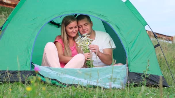 Milující muž dal sedmikrásky, zatímco seděl ve stanu při kempování. — Stock video