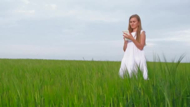 Vrouw boer met een tablet staat op een veld van groene tarwe. — Stockvideo