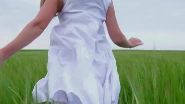 En ung flicka springer över ett grönt vetefält i en vit klänning. Långsamma rörelser. — Stockvideo