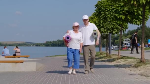 可爱的老夫妇带着瑜伽垫沿着海滨散步。友好气氛. — 图库视频影像