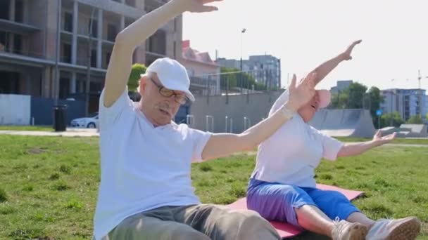 Älteres Paar treibt Sport auf einer Matte im Park.