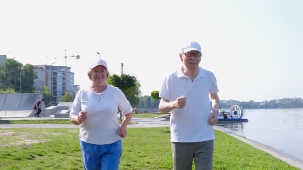 Los abuelos hacen un entrenamiento matutino junto al lago. Las personas mayores corren para recuperar energía. — Vídeo de stock