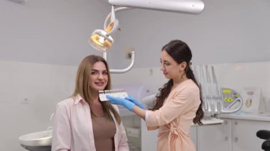 Bir dişçi modern bir klinikte bir hastaya danışır. Kozmetik gülümseme için bir gölge rehberi kullanır.