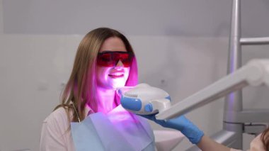 Bir kadın modern ve gelişmiş bir diş sağlığı kliniğinde diş beyazlatma prosedüründen geçiyor.