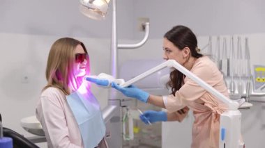 Bir kadın modern ve modern bir diş kliniğinde LED kullanılarak profesyonel diş beyazlatma prosedürüne tabi tutuluyor..
