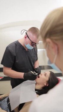 Profesyonel bir diş hekimi, modern bir klinikte hastaya diş sağlığı, hassasiyet ve tıbbi uzmanlığı vurgularken, ayrıntılı bir sözlü muayene yapar..