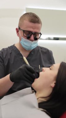 Profesyonel bir diş hekimi, ağız sağlığı, hijyen ve profesyonel bakımı vurgulayarak, temiz ve modern bir klinikte rutin bir diş kontrolü sırasında hastayı dikkatlice muayene eder..