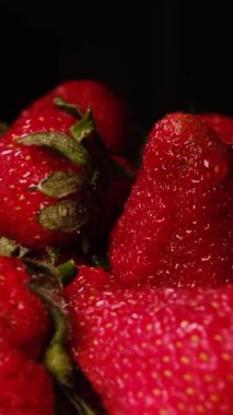 Koyu arkaplanda taze kırmızı çileklerin yakın plan çekimi, sulu dokularını, doğal tazeliklerini ve canlı renklerini vurguluyor..