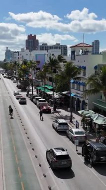 Güneşli bir günde Florida 'da samimi kafeleri, palmiye ağaçları ve modern otelleri olan zengin bir Miami Beach caddesi manzarası..