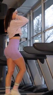 Parlak, modern bir spor salonunda koşu bandında egzersiz yapan, aktif ve sağlıklı bir yaşam tarzı sürdüren genç bir kadının sabah sporu..