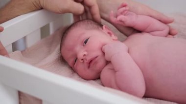 Sevimli yeni doğmuş bebek beşikte dinleniyor, sakince yukarı bakıyor. Yumuşak ışık ve pastel renkler sıcaklıkla, masumiyetle ve erken yaşam güzelliğiyle dolu huzurlu bir atmosfer yaratır..