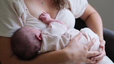 Evde yeni doğmuş bebeğine sarılan bir annenin yakın çekimi. Yumuşak duygu, sıcak aydınlatma ve barışçıl kompozisyon rahatlık, güvenlik ve erken anneliğin güzelliğini ifade eder..