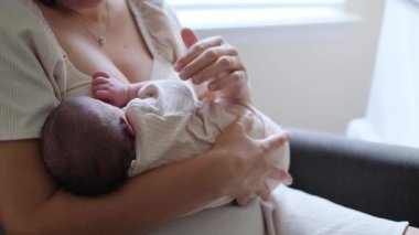 Bir annenin, parlak bir odada bir kanepede otururken uyuyan bebeğini kucakladığı huzurlu bir an. Yumuşak ışık ve doğal duygu, sakin sevgi ve annelik şefkatini yansıtır..