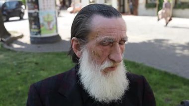 Beyaz sakallı yaşlı bir adam gözlerini kapalı bir bankta dinleniyor, sakin bir rahatlama ve yansıma anı yakalıyor..
