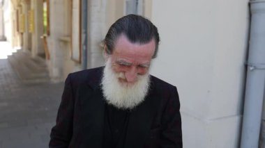 Gri saçlı yaşlı bir adam, modern şehir binalarıyla dolu güneşli bir cadde boyunca yürüyor. Huzurlu bir an, bağımsızlığı, yaşlanmayı ve günlük hayatın basit güzelliğini yansıtıyor..