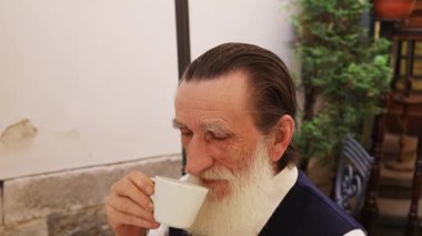 Uzun beyaz sakallı, kırsal bir duvara ve yeşilliğe bakan yaşlı bir adamın yakın plan portresi yansıtıcı bir ruh hali içinde..