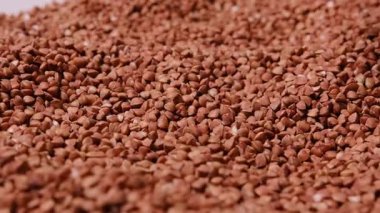 Ham karabuğdayın detaylı makro görüntüleri yumuşak ışık altında yavaşça dönüyor, kumlu dokuyu, kahverengi rengi ve sağlıklı organik besinleri vurguluyor..