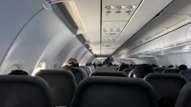 Geniş koridor ve yumuşak ortam aydınlatmasıyla aydınlatılan rahat koltukları olan modern uçak içi geniş kabin tasarımı ve rahat seyahat atmosferini gözler önüne seriyor..