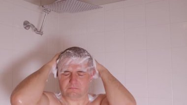 Adamın duş altında saçlarını şampuan köpüğüyle yıkadığı yakın çekim videosu. Hijyen, kişisel bakım ve sabah rutini kavramı.