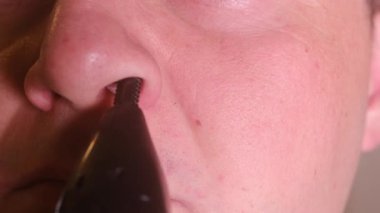 Bir adamın burun kıllarını tımar etmek için elektrikli budayıcı kullanırken, kişisel hijyen ve yüksek çözünürlüklü tımar yaparken yakın çekim makro videosu..