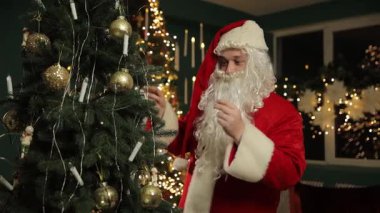 Noel Baba nazikçe ışıldayan bir Noel ağacına süslerini yerleştirir. Etrafı festival ışıkları ve sıcak tatil atmosferiyle çevrilidir..