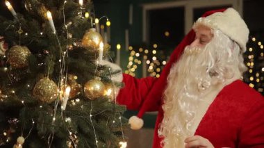 Noel Baba Noel ağacını parlak süsler ve altın ışıklarla süslüyor, neşeli tatil ruhunu yayıyor..