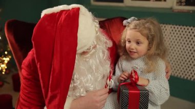 Noel Baba 'ya sıcak bir Noel parıltısıyla bakarken elinde bir hediye tutan kız..