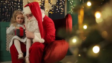 Noel Baba, hediyeler ve ışıklarla dolu parıldayan bir Noel ağacının yanında gülümseyen çocuklarla neşeli vakit geçirir..