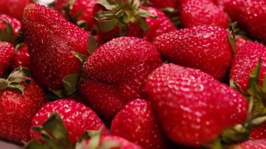 Olgun çileklerin sulu kırmızı yüzeyi, küçük tohumları ve taze yaprakları yakından gösteren makro videosu. Yemek, beslenme ve yaz temaları için mükemmel..