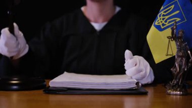 Siyah cüppeli yargıç duruşma sırasında tokmağına vurdu. Masadaki Ukrayna bayrağı ve Adalet Heykeli hukuku, otoriteyi ve adil yargılamayı simgeliyor..