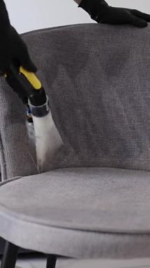 Gri kumaş bir koltuğun koltuğunu temizleyen sökücü nozülün yakın çekimi.