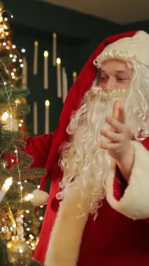 Noel Baba elini sıcak ışıklarla süslenmiş bir Noel odasında sallıyor..