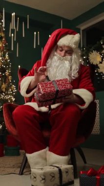 Noel Baba rahat bir Noel salonunda, bir koltukta hediyesini sarmalayarak rahatlar..