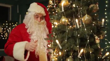 Noel Baba, güzel dekore edilmiş Noel ağacının altına sıcak tatil ışıklarıyla parlayan hediyeler yerleştirmek için eğilir..