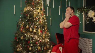 Noel ağacının yanında duran bir adam Noel Baba 'yı oynadığı yorucu ve uzun bir günün ardından saçını düzeltirken, arkasında ılık festival ışıkları yavaşça parlıyor..