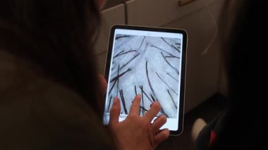 Bir trichologist, modern bir klinikte profesyonel bir saç ve kafa derisi muayenesi sırasında dijital tablette yakın çekim kafa taraması gösteriyor..