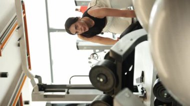 Modern bir spor salonunda kadın halterlerini kaldırıyor. Dikey video.