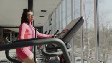 Pembe elbiseli bir kadın modern bir spor salonunda koşu bandında tren kullanıyor. Bu kardiyo egzersizi dayanıklılığı, dayanıklılığı ve genel uygunluğu arttırır..