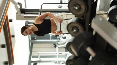 Bir kadın spor salonunda elleriyle çekerken bacaklarının etrafına elastik bir halka bandıyla güç egzersizi yapıyor..