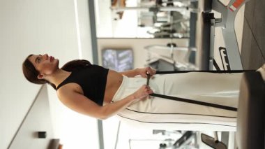 Kadın modern bir spor salonunda dimdik ayakta duruyor ve direnç kabloları ya da bantlarla güç egzersizi yapıyor..