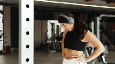 Kadın elbiselerini ayarlıyor ve spor salonunda egzersiz rutinine hazırlanıyor. Tüm vücut eğitimine başlamadan önce doğal hareketler.