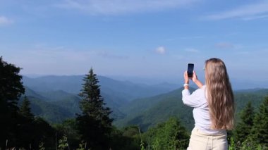 Bir kadın telefonunu kaldırıp Amerika 'daki açık mavi gökyüzünün altındaki manzaralı tepeleri yakalamak için dağlara bakıyor..